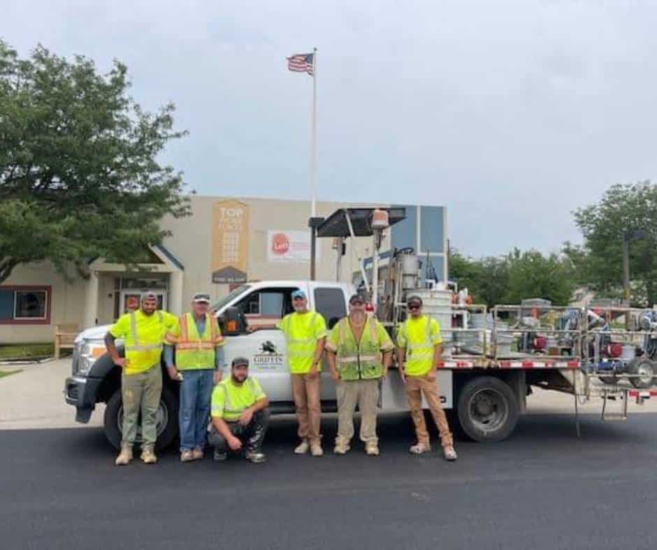 Workers posing in front of a smaller pavement marking truck.